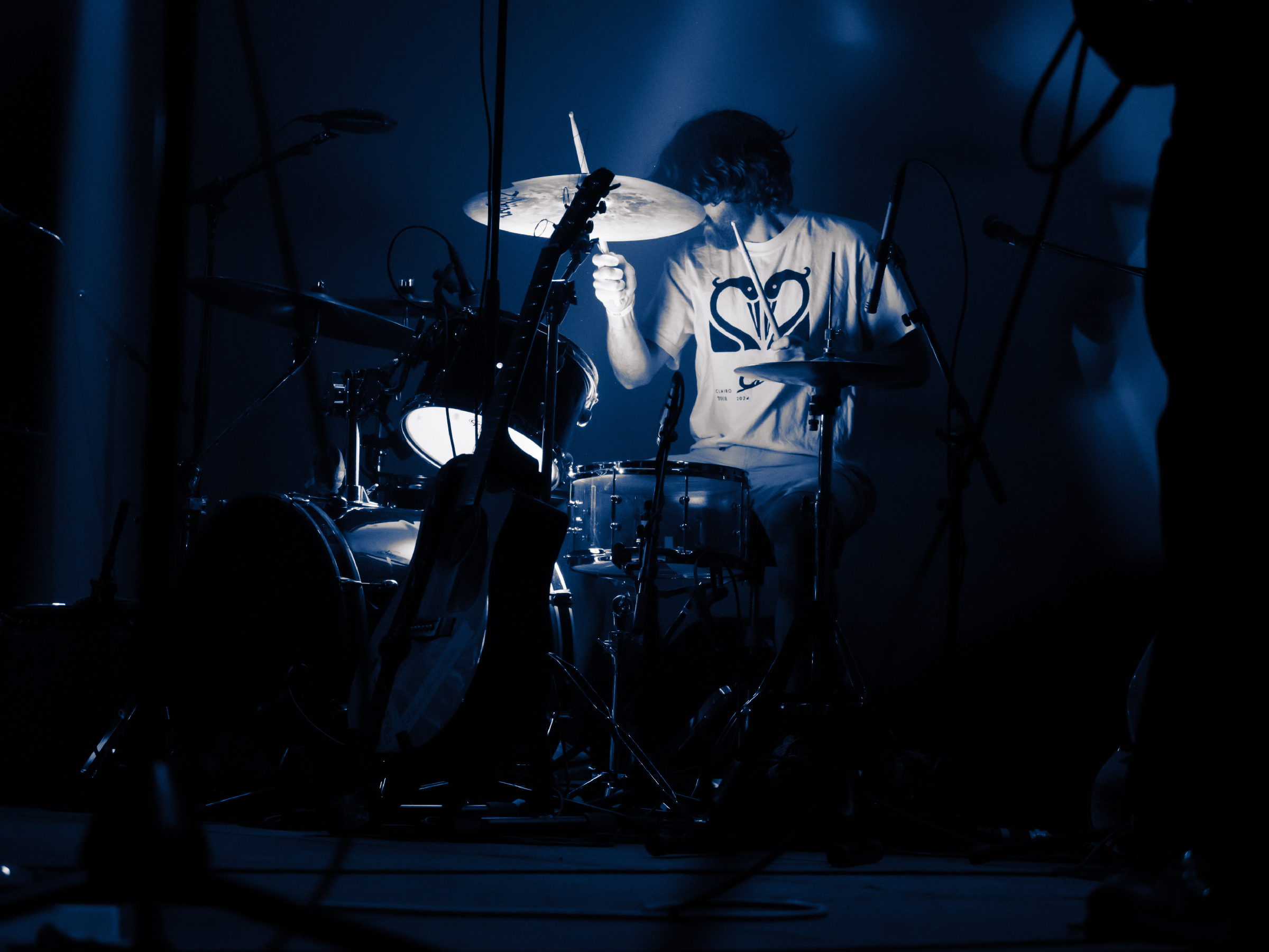 Brendan plays drums, lit by a light beneath the drums. His own shadow assumes an imposing position behind him.