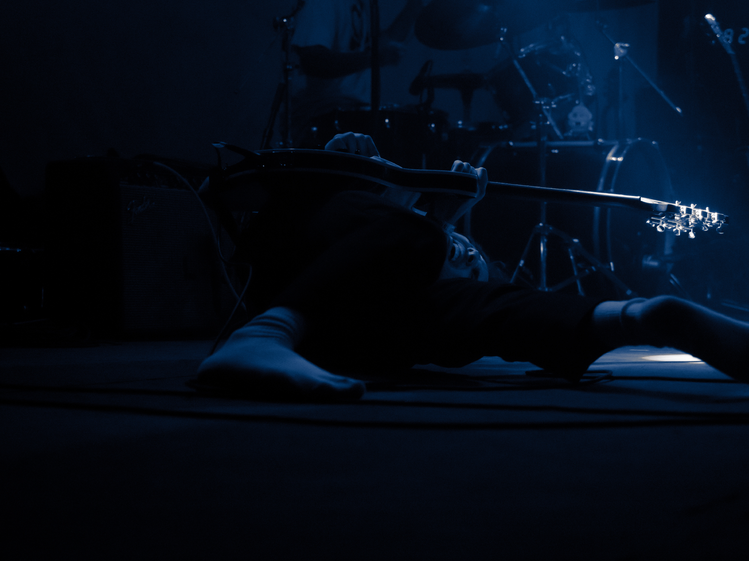 Trevor rolls around on stage. His face is framed by the neck of the guitar and his left leg.