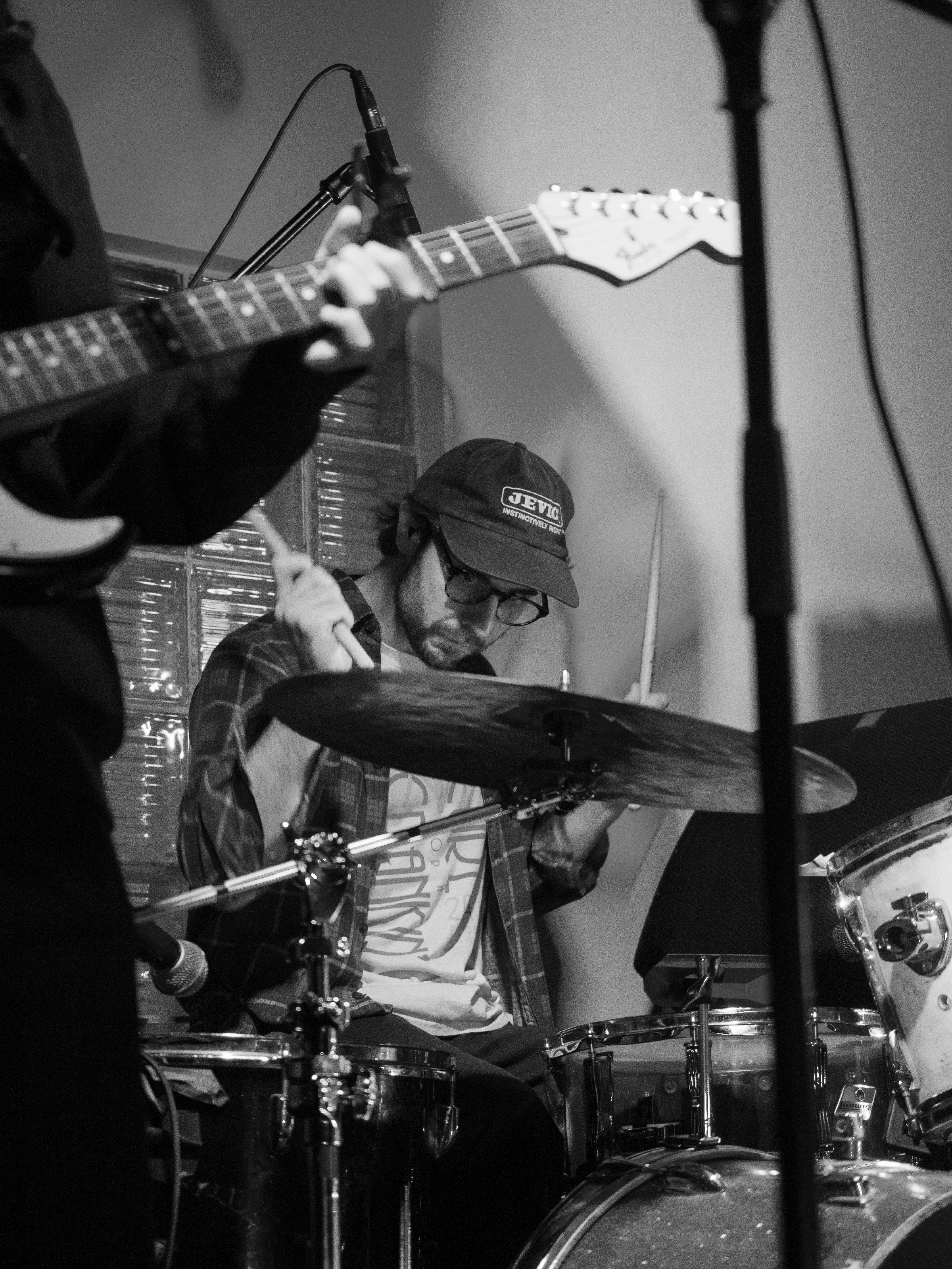 Sam plays drums. His face is framed by Nara's guitar and his own sticks.