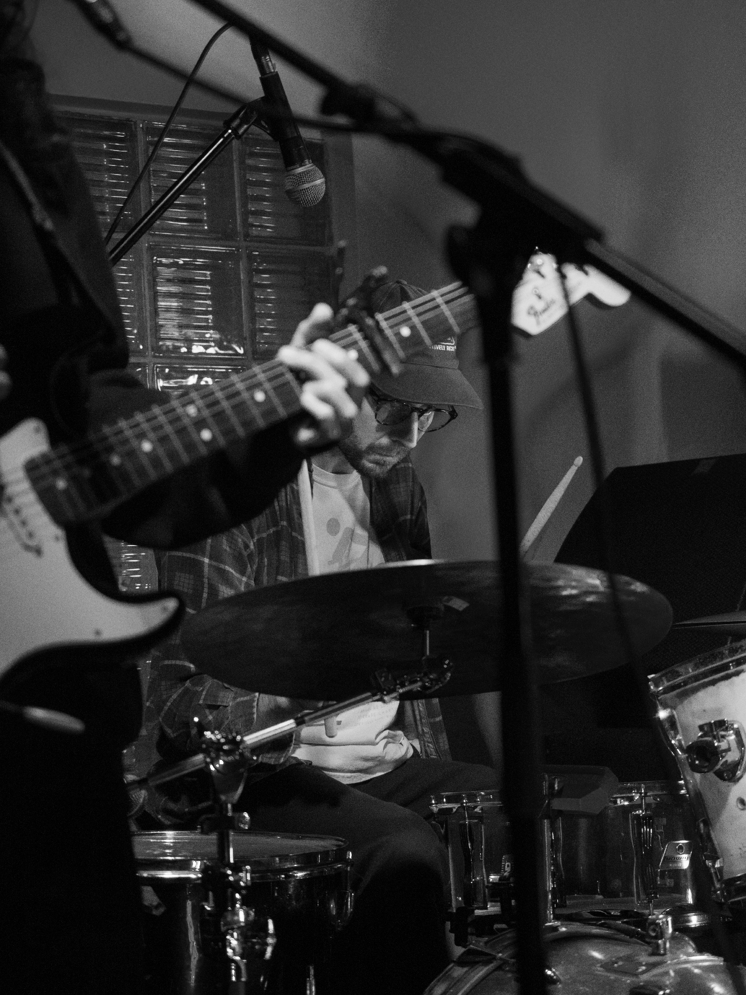 Sam plays drums. His face is framed by Nara's guitar.