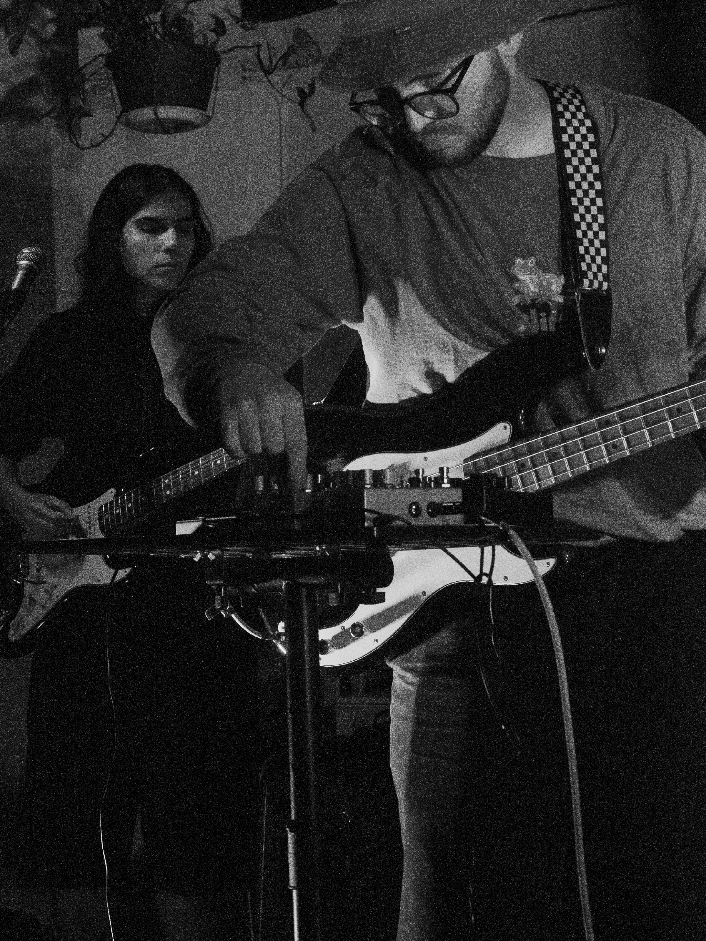 Will fiddles with pedals in the foreground. His head and shoulders frame Nara in the background.